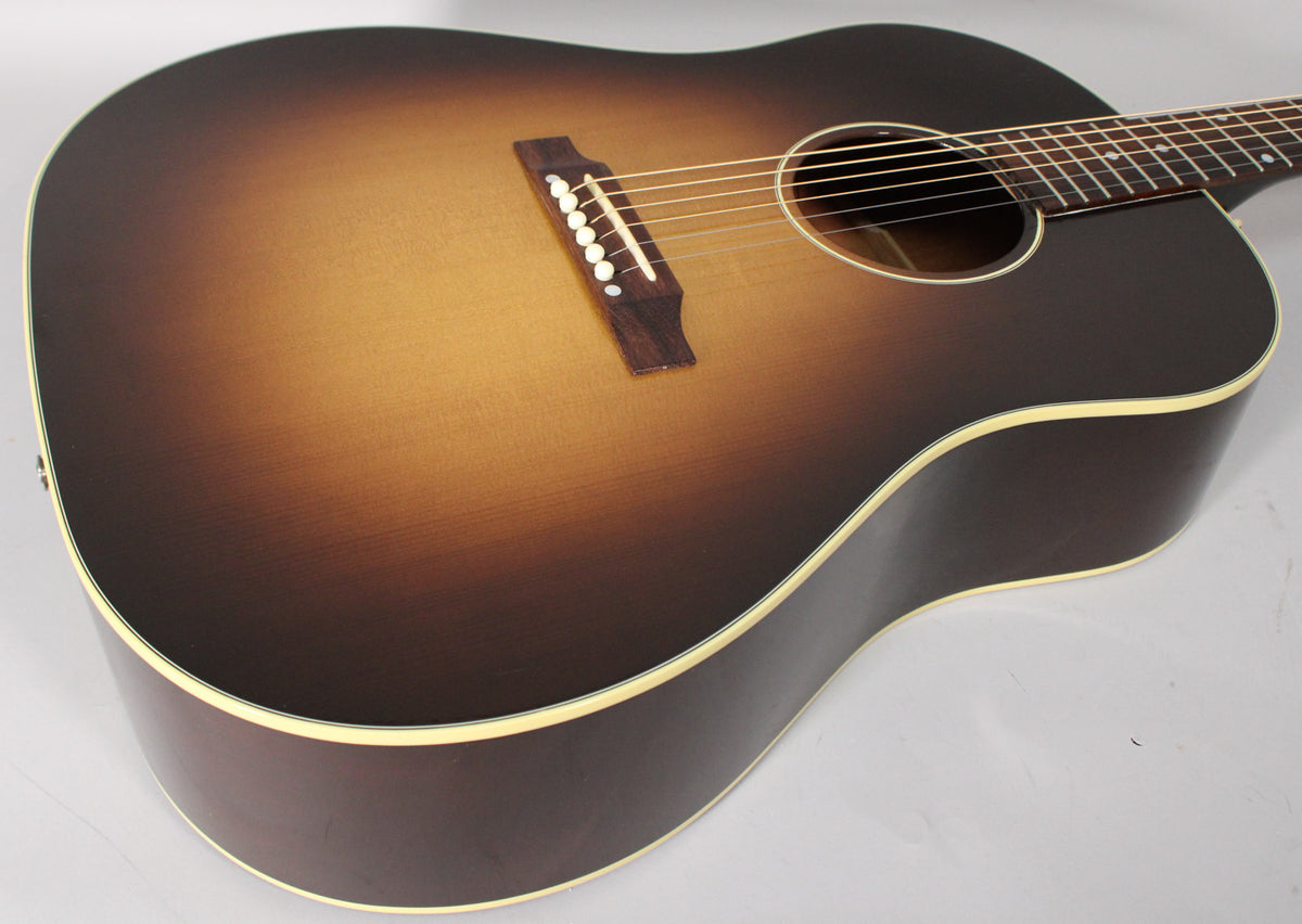 The acoustic guitar's body, in a matte vintage sunburst finish, is angled from the lower bout to the soundhole, showing the bridge.