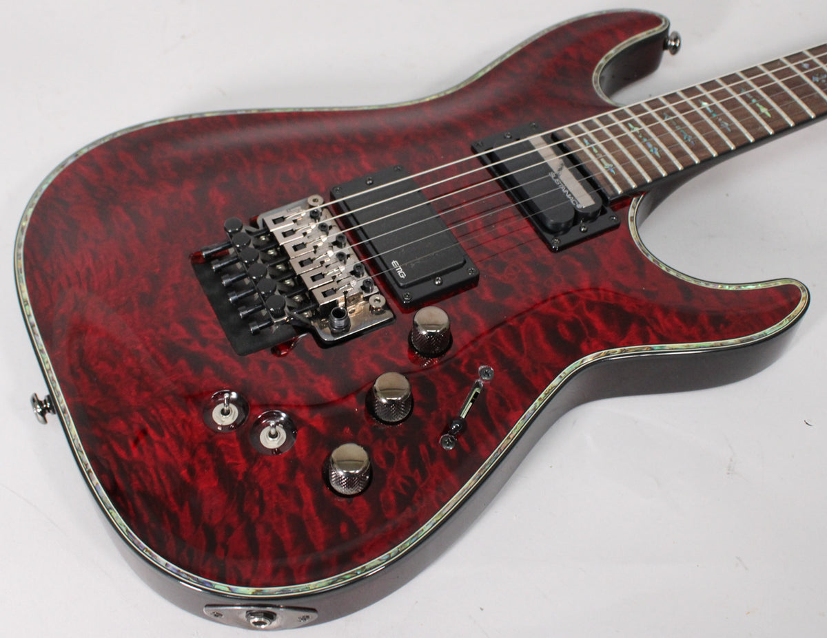 Close-up of a deep red quilted maple guitar body with black hardware, abalone binding, and three chrome knobs, viewed from above.
