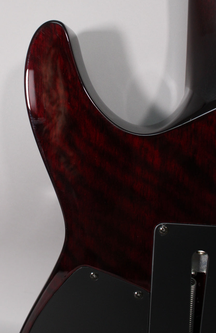 Close-up of the guitar's upper horn and cutaway, showing the black cherry quilted maple finish with light scratches and the tremolo cavity cover.
