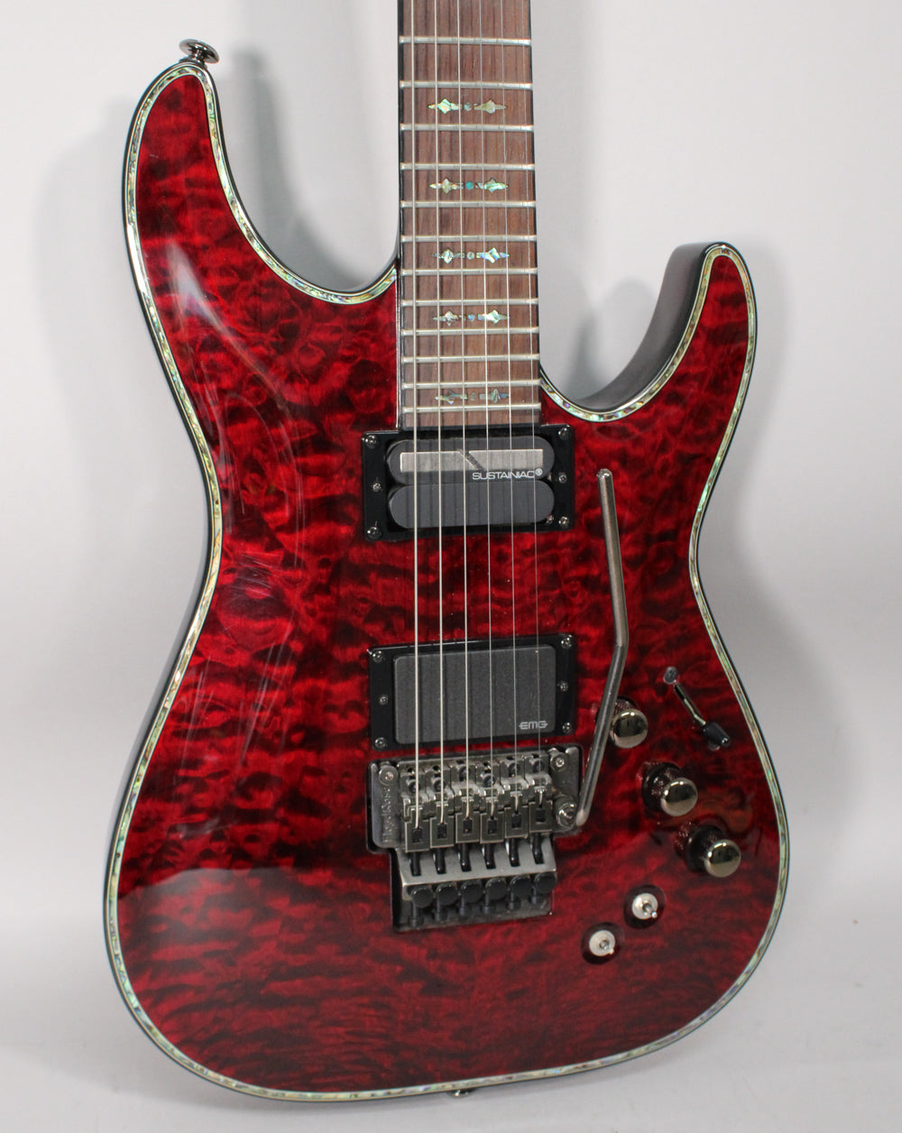 Close-up of a red quilted maple electric guitar with a Floyd Rose tremolo, two humbuckers, and abalone binding.