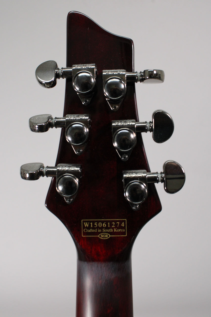 The back of a dark cherry red guitar headstock with six chrome tuners, showing a serial number sticker.