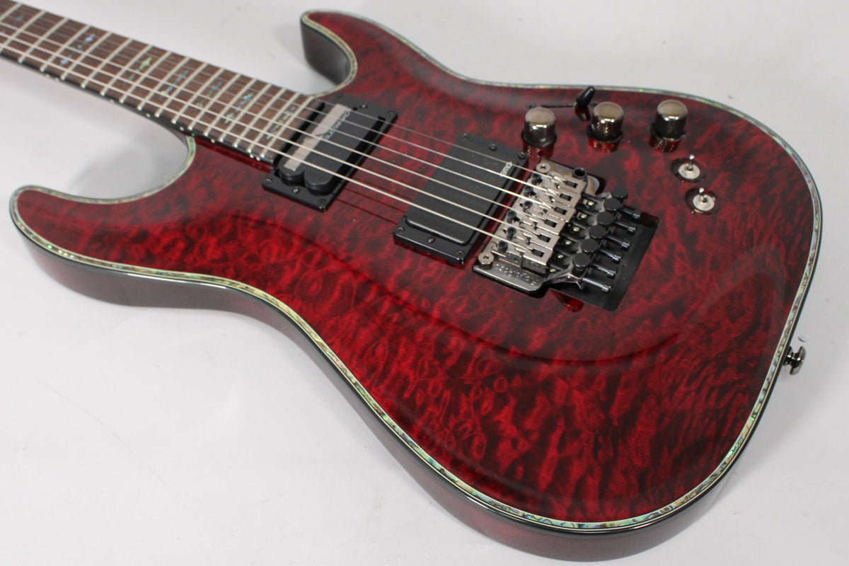 The upper body of a dark cherry red quilted maple guitar, showing the black pickups, Floyd Rose tremolo, and abalone binding.
