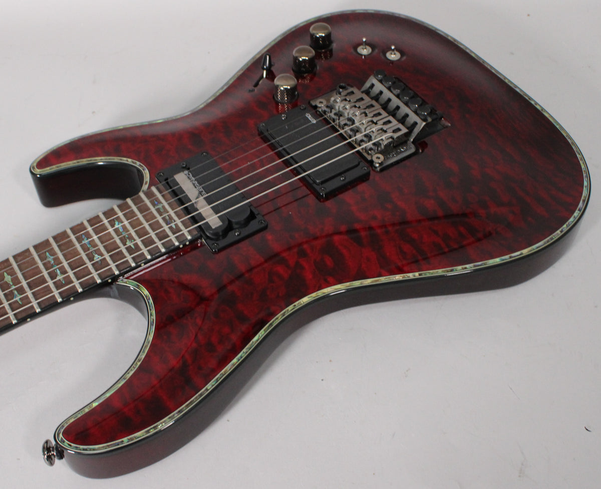 The guitar's dark cherry burst finish with quilted maple top is visible from the upper bout, showing black hardware and abalone binding.