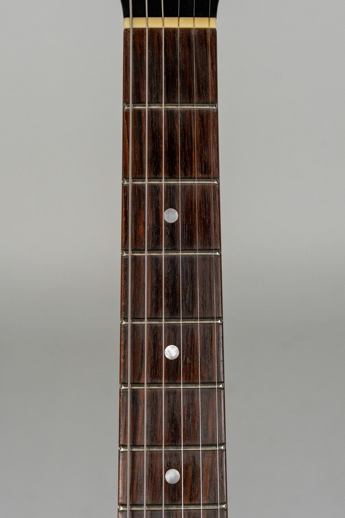 Close-up of the guitar's dark rosewood fretboard with six strings, metal frets, and three circular pearloid inlays.