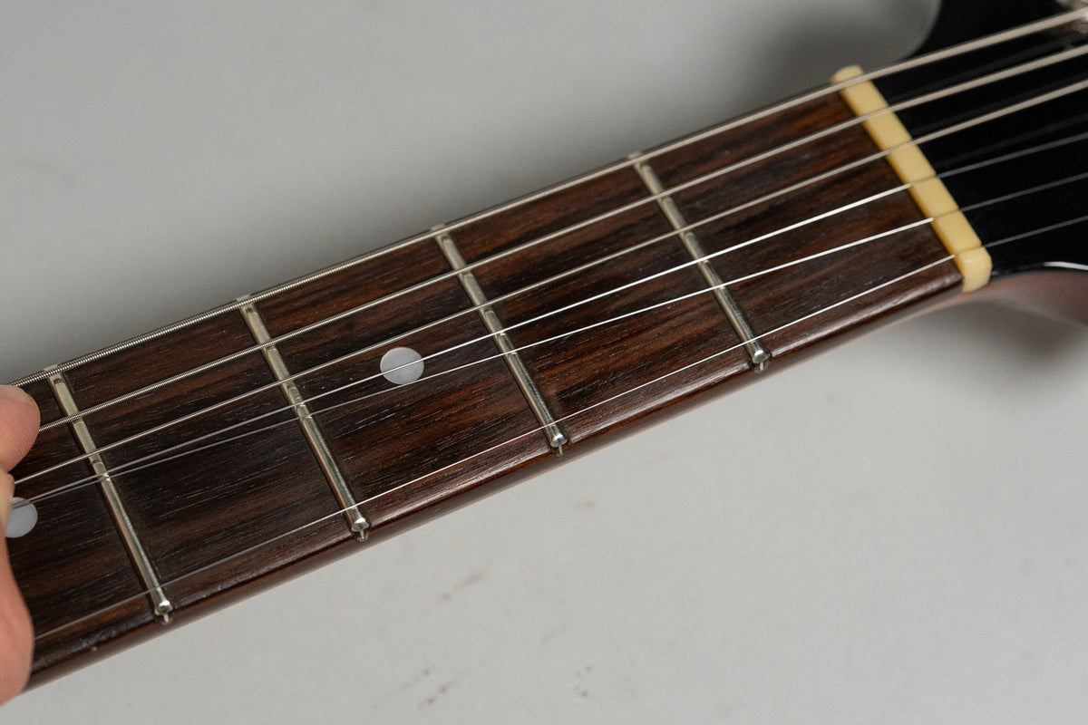 Close-up of the dark rosewood fretboard with white dot inlays and a cream-colored nut, showing light wear on the frets.