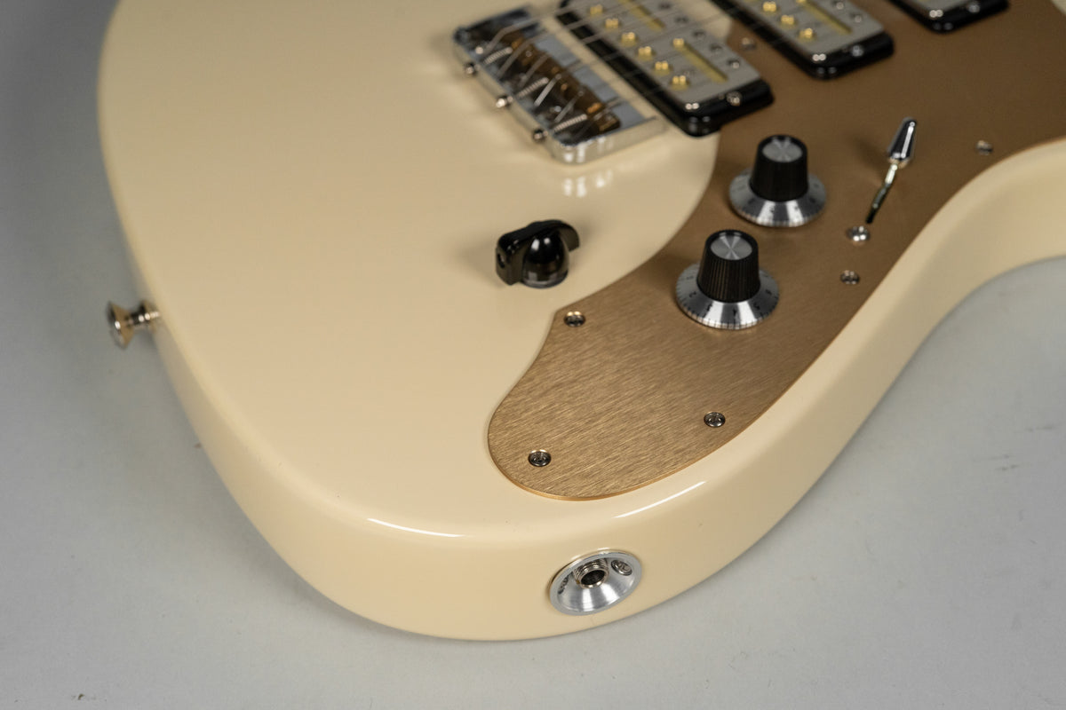 Close-up of the lower bout, showing the antique white finish, brushed gold control plate with two black knobs, and output jack.