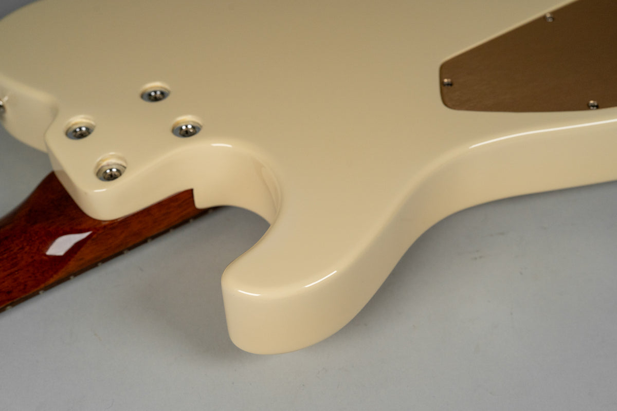 The guitar's antique white body, with a brown control cavity cover, meets a dark wood neck with a white inlay.
