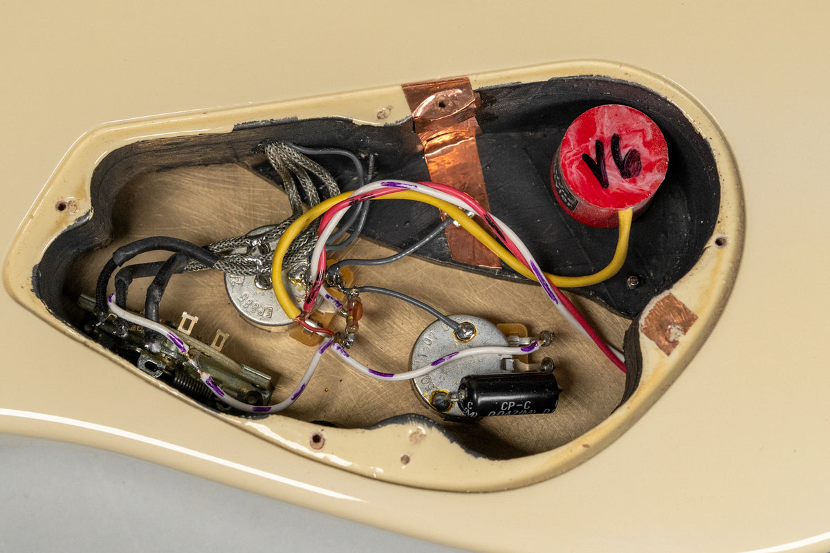 Close-up of the guitar's wiring cavity, showing pots, capacitors, and a red circular component with "V6" written on it.