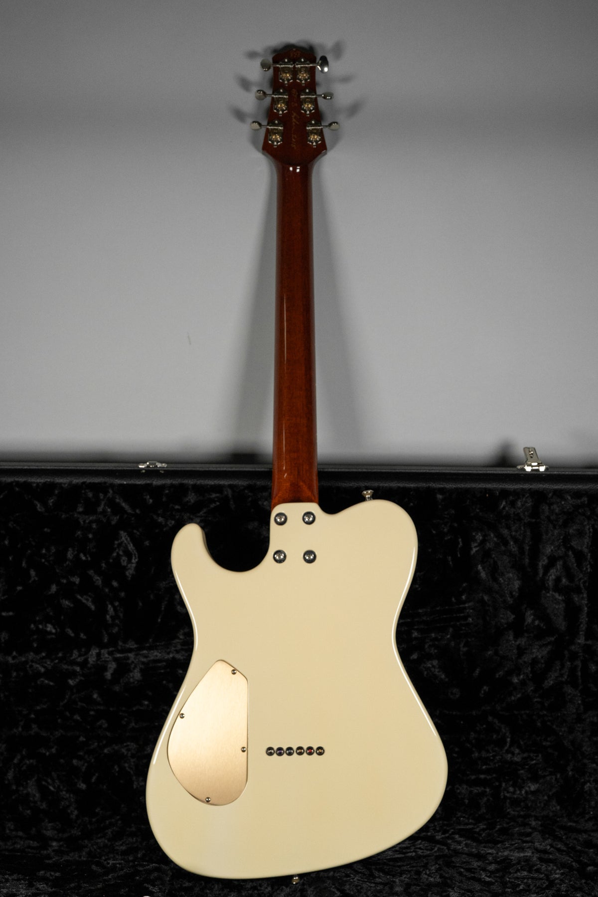 The guitar's back is antique white with a gold control plate, six string ferrules, and a dark brown neck and headstock.