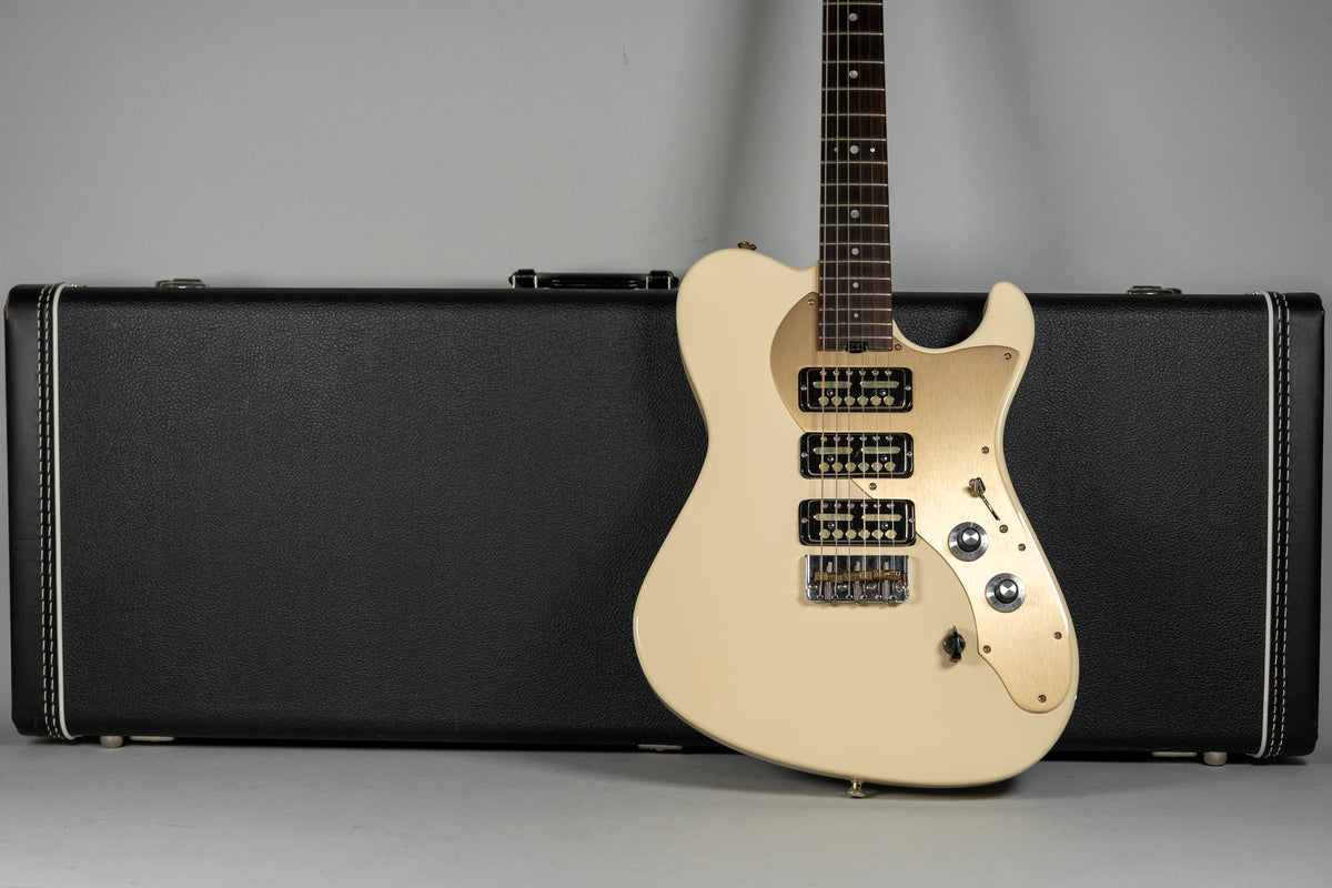 Antique white electric guitar with a gold pickguard and three gold foil pickups, leaning against a black hard case.