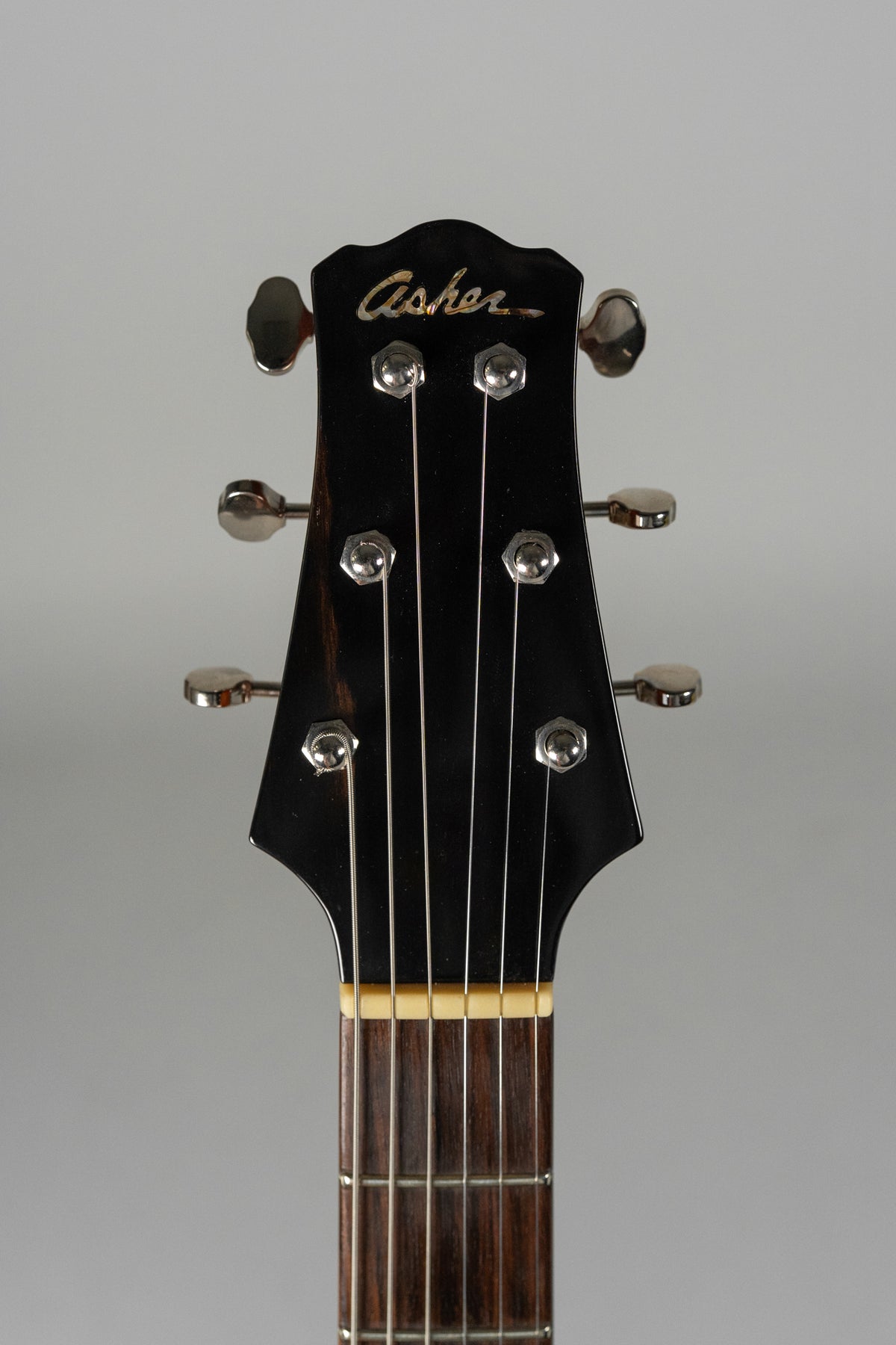 Close-up of the guitar's black headstock with six chrome tuners, a cream nut, and the top of the dark fretboard.