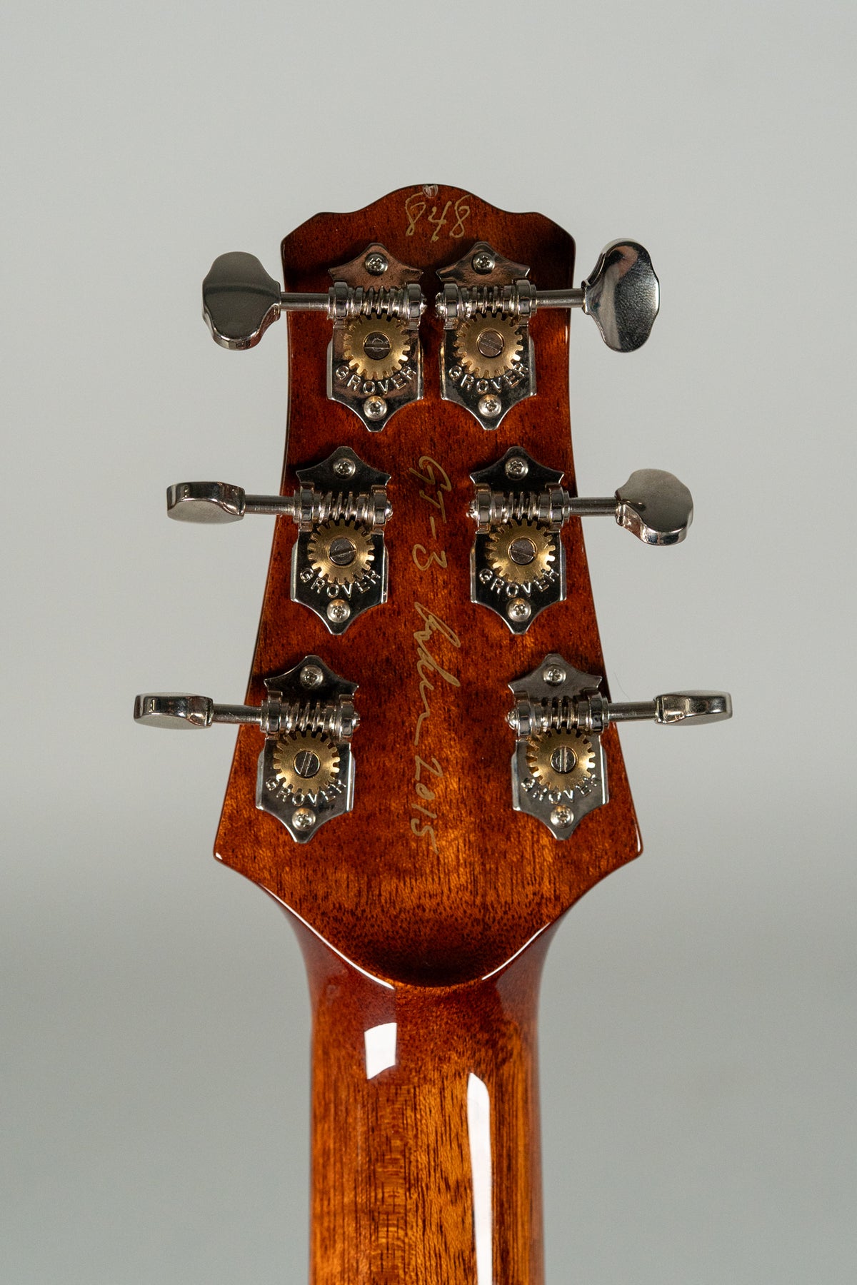 The back of a glossy, reddish-brown headstock with six chrome tuners, each with a brass gear and "GROVER" stamped on the plate.