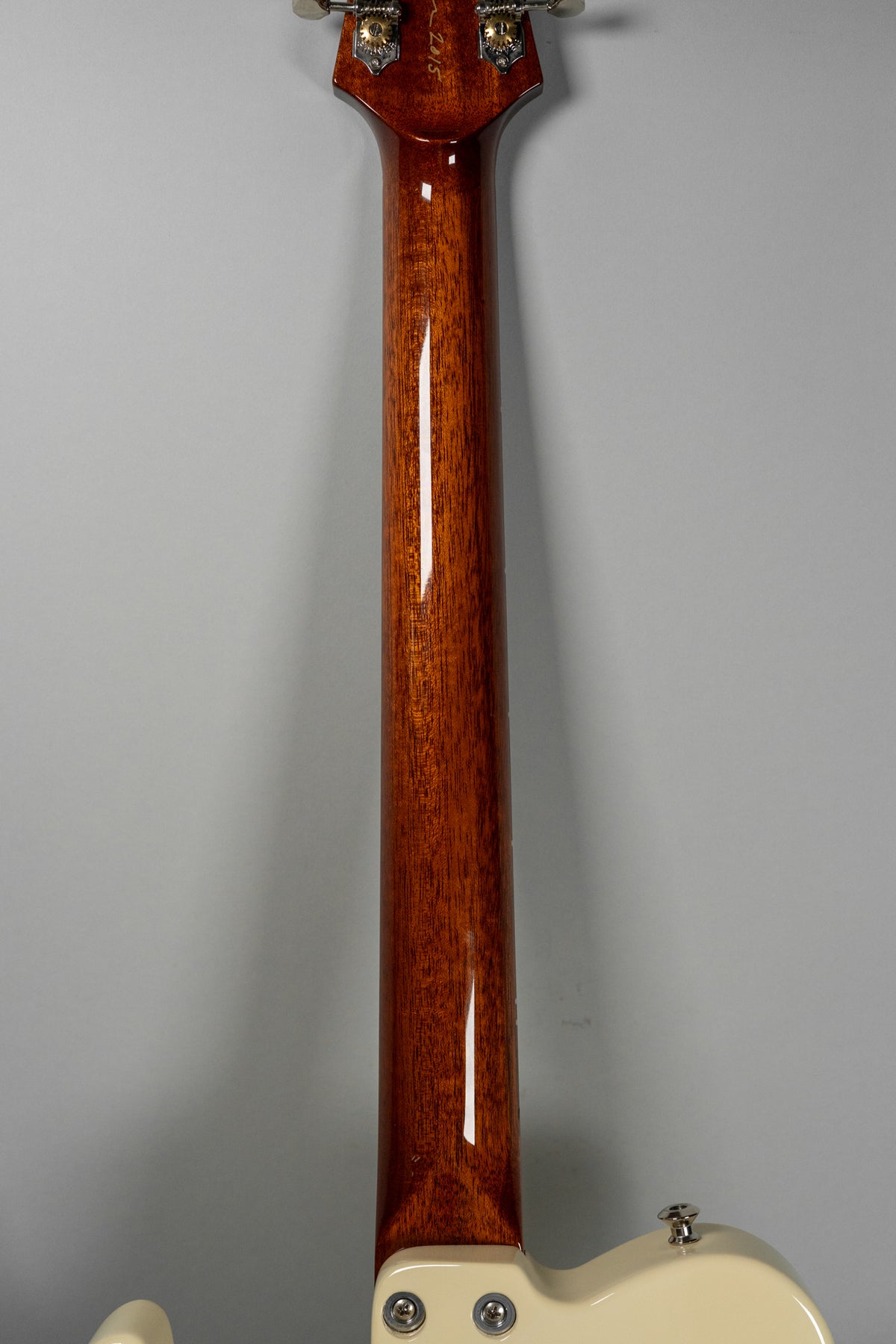 The guitar's glossy, dark reddish-brown neck and headstock are viewed from behind, with a cream body visible at the bottom.