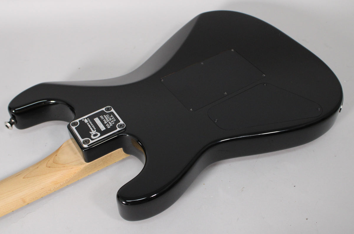 The guitar's glossy black body is viewed from the back, showing the neck joint, a light maple neck, and two control cavity covers.