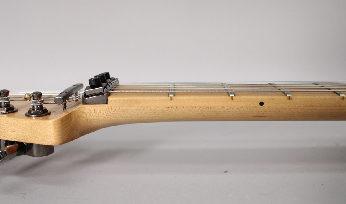 The guitar's light maple neck and fretboard are viewed from the side, showing dark tuning pegs and a locking nut at the headstock.