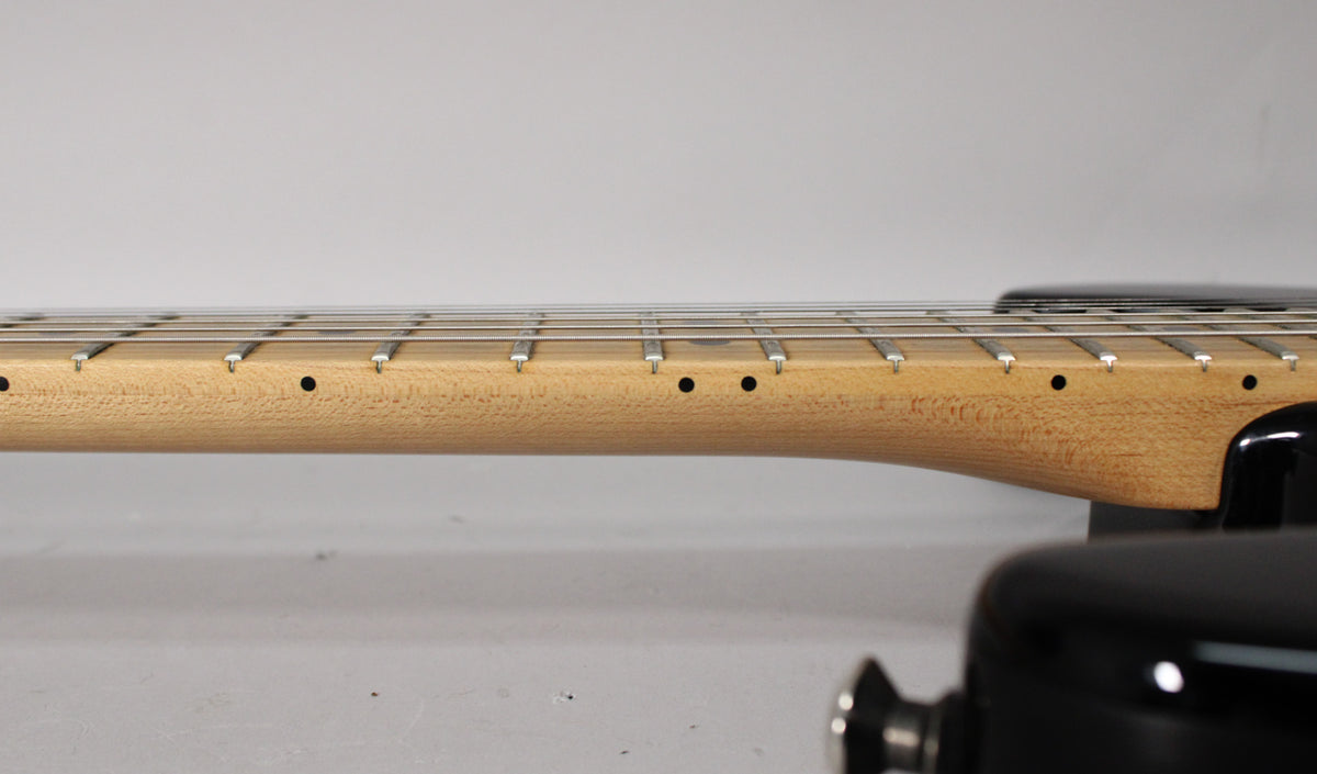 Close-up of the guitar's maple neck and fretboard, showing the side dot markers and frets, with a black strap button visible.