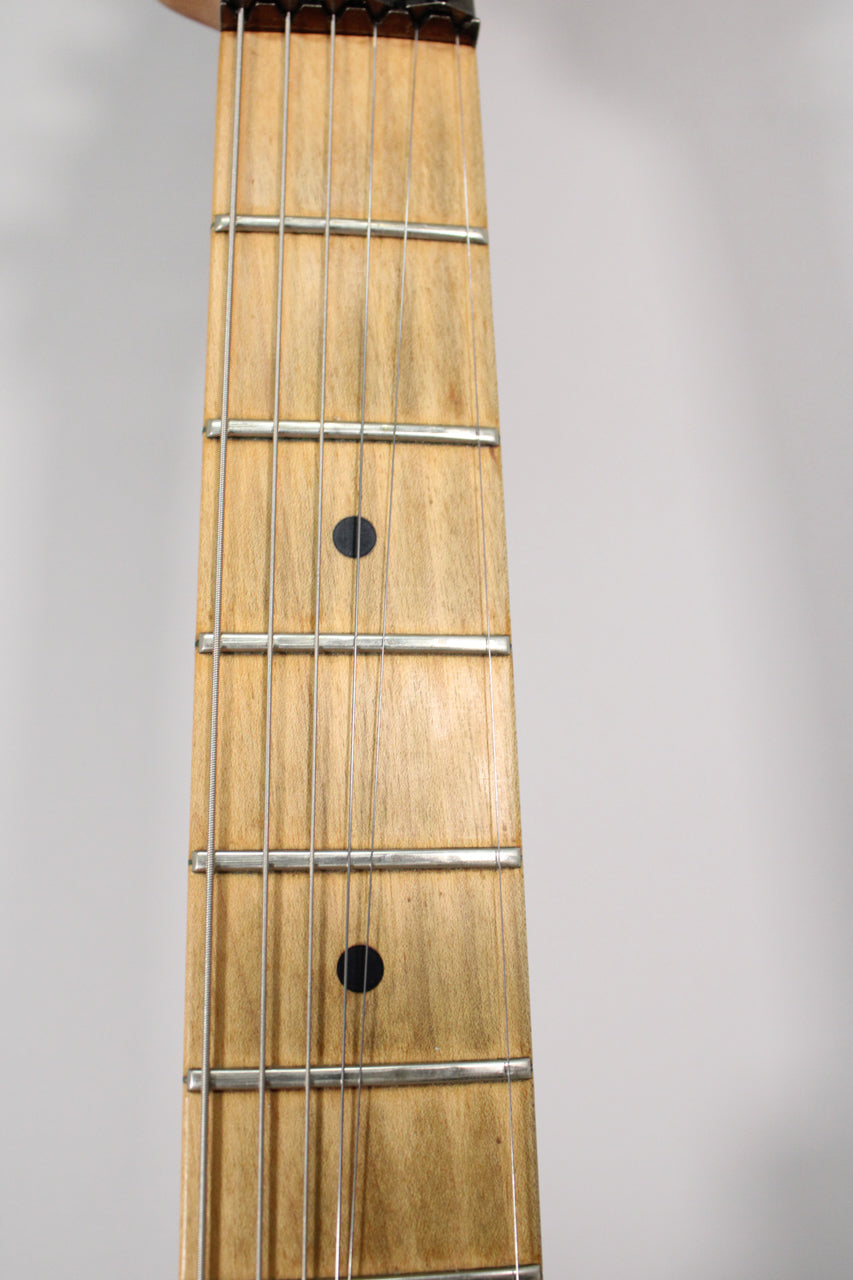 Close-up of the light wood fretboard with dark circular inlays, showing six strings and silver frets, with some visible wear.