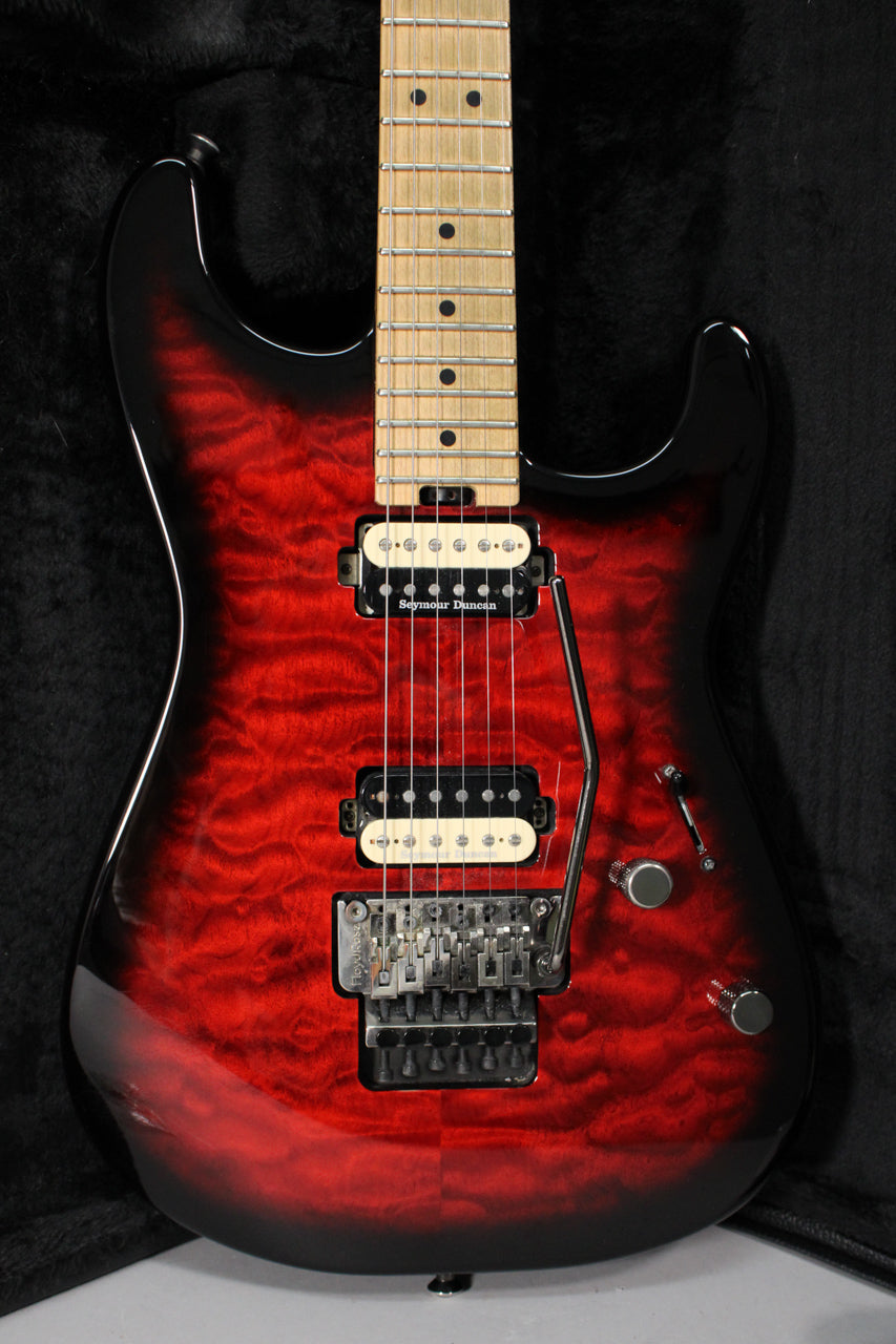 The guitar's body, in transparent red burst with black edges, shows a maple fretboard, two humbuckers, a Floyd Rose bridge, and two control knobs.