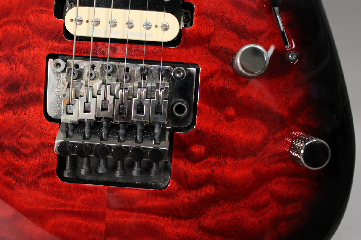 Close-up of the guitar's lower body, showing the transparent red burst finish, a Floyd Rose tremolo system, and two chrome control knobs.