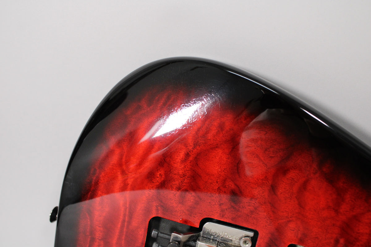 Close-up of the guitar's upper bout, showing the transparent red burst finish with visible wood grain and a Floyd Rose tremolo.