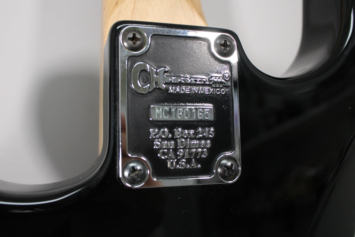 Close-up of the guitar's black body and light wood neck, showing the chrome neck plate with four screws and engraved text.