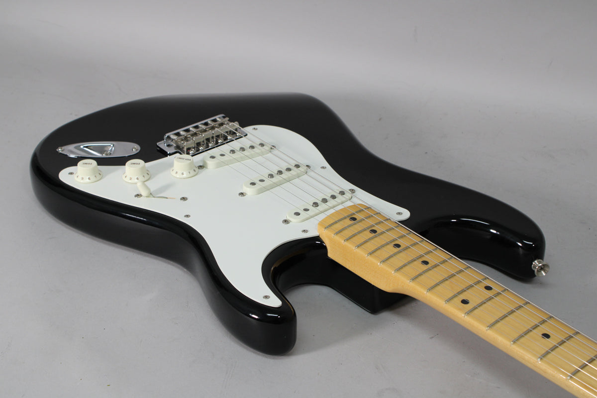 Black Stratocaster with a white pickguard, three single-coil pickups, three cream control knobs, and a maple neck, viewed from above.