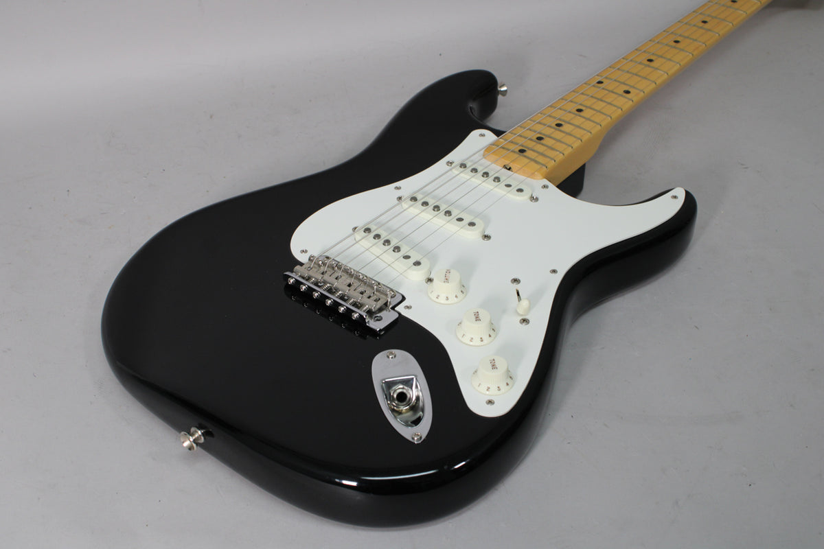 Black Stratocaster, angled from above, showing the glossy body, white pickguard, three single-coil pickups, and maple fretboard.