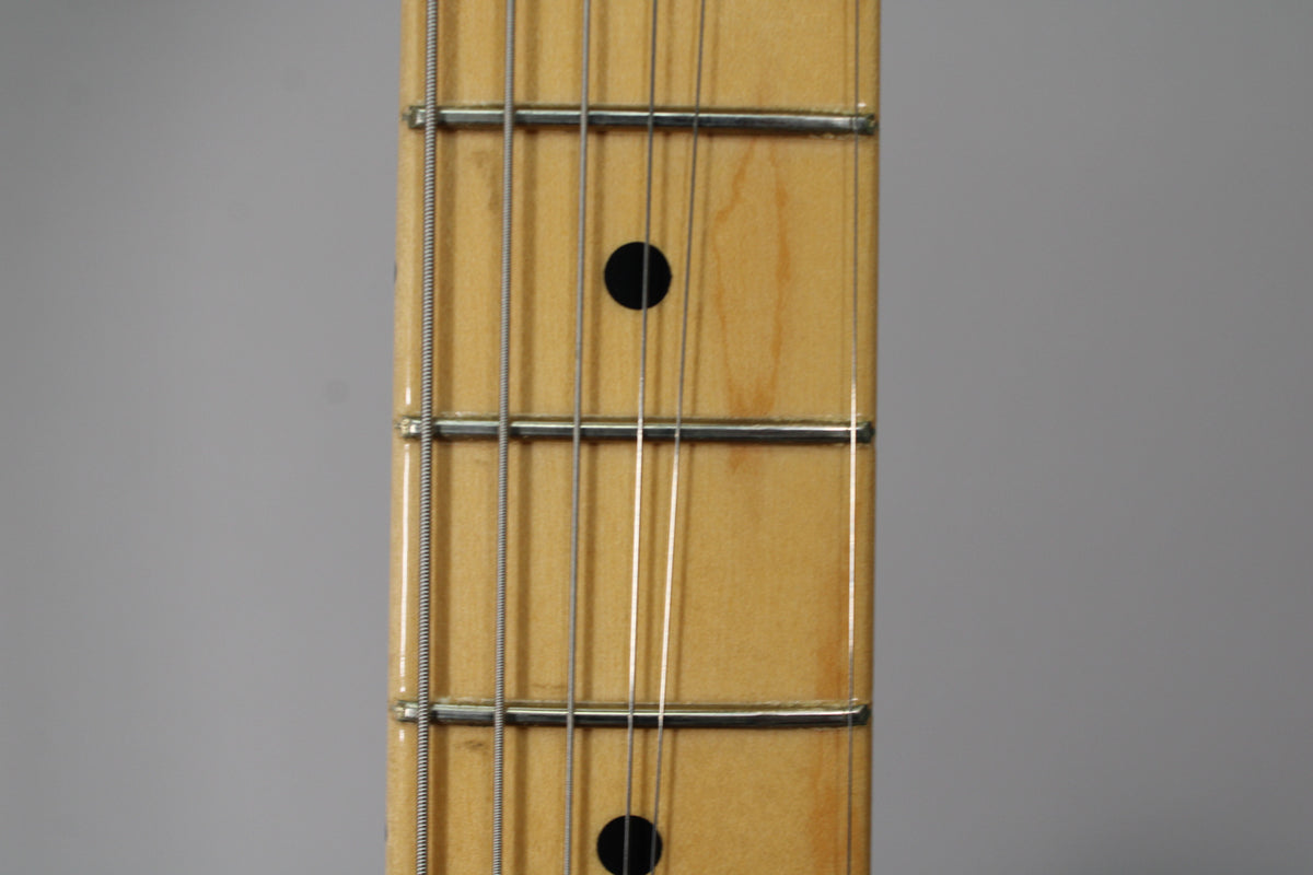 Close-up of the maple fretboard, showing black dot inlays, frets, and strings, with light wear on the wood.
