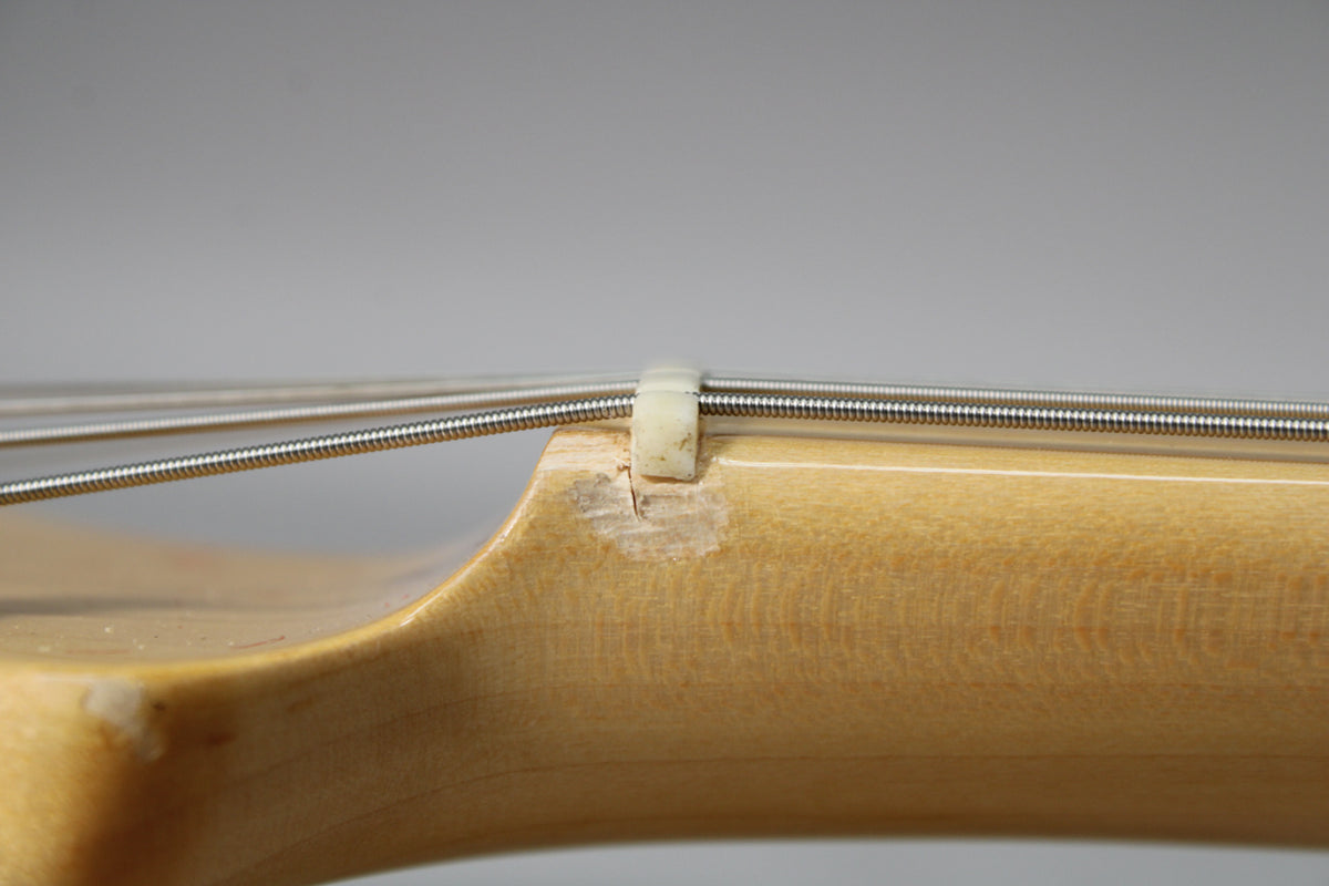 Close-up of the guitar's light-colored neck and strings, showing a chipped nut and finish wear at the headstock joint.