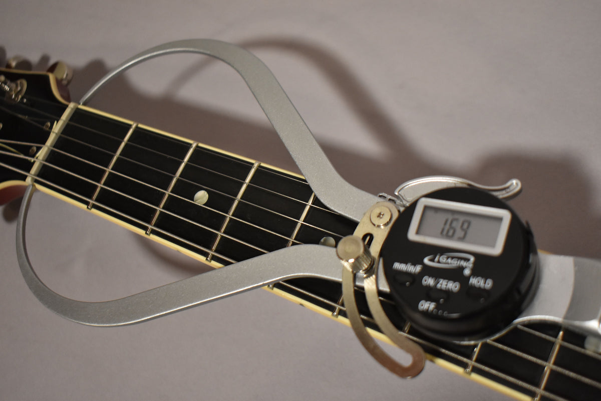 A digital caliper measures the guitar's nut width at 1.69 inches, showing the dark fretboard and cream binding.