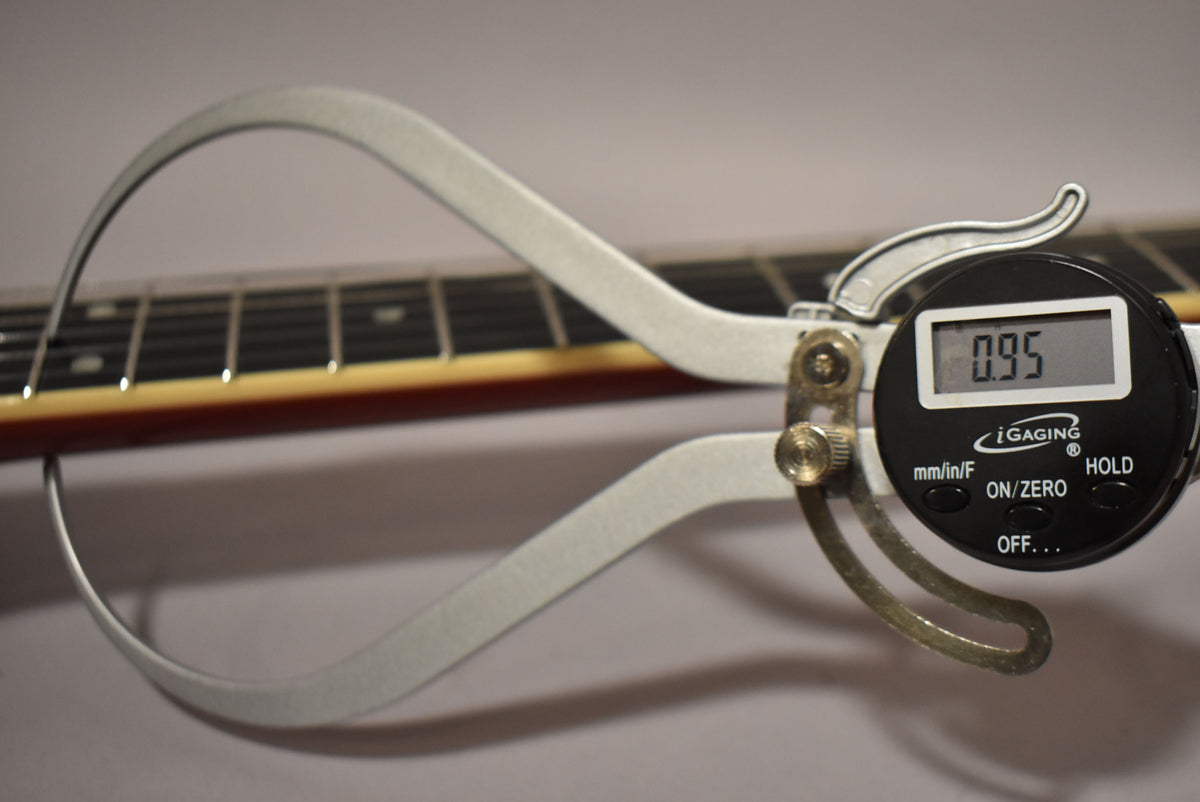A digital caliper measures the guitar's neck thickness at 0.95, showing the frets and binding of the cherry burst finish.