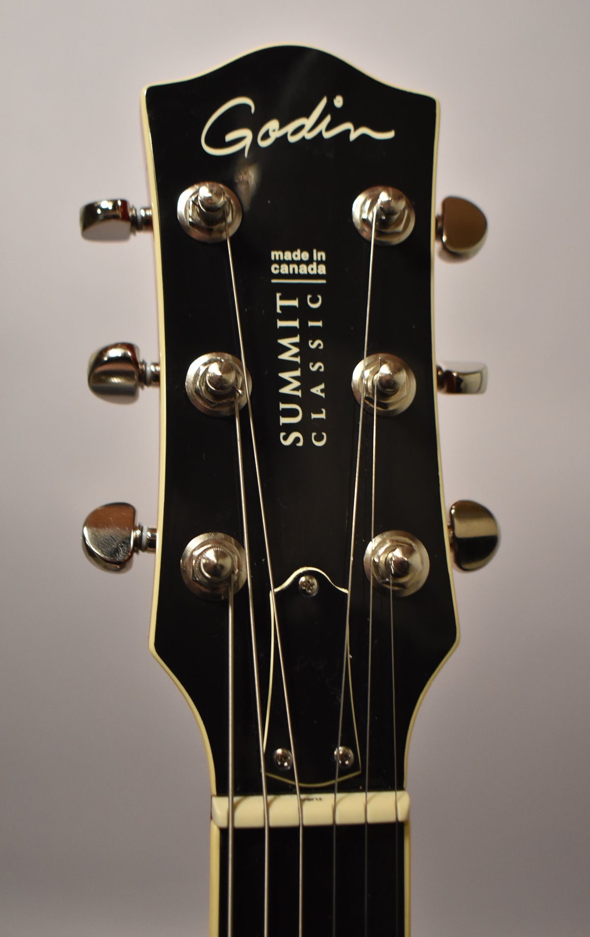 Close-up of the guitar's black headstock with cream binding, showing six chrome tuners, a white nut, and strings.