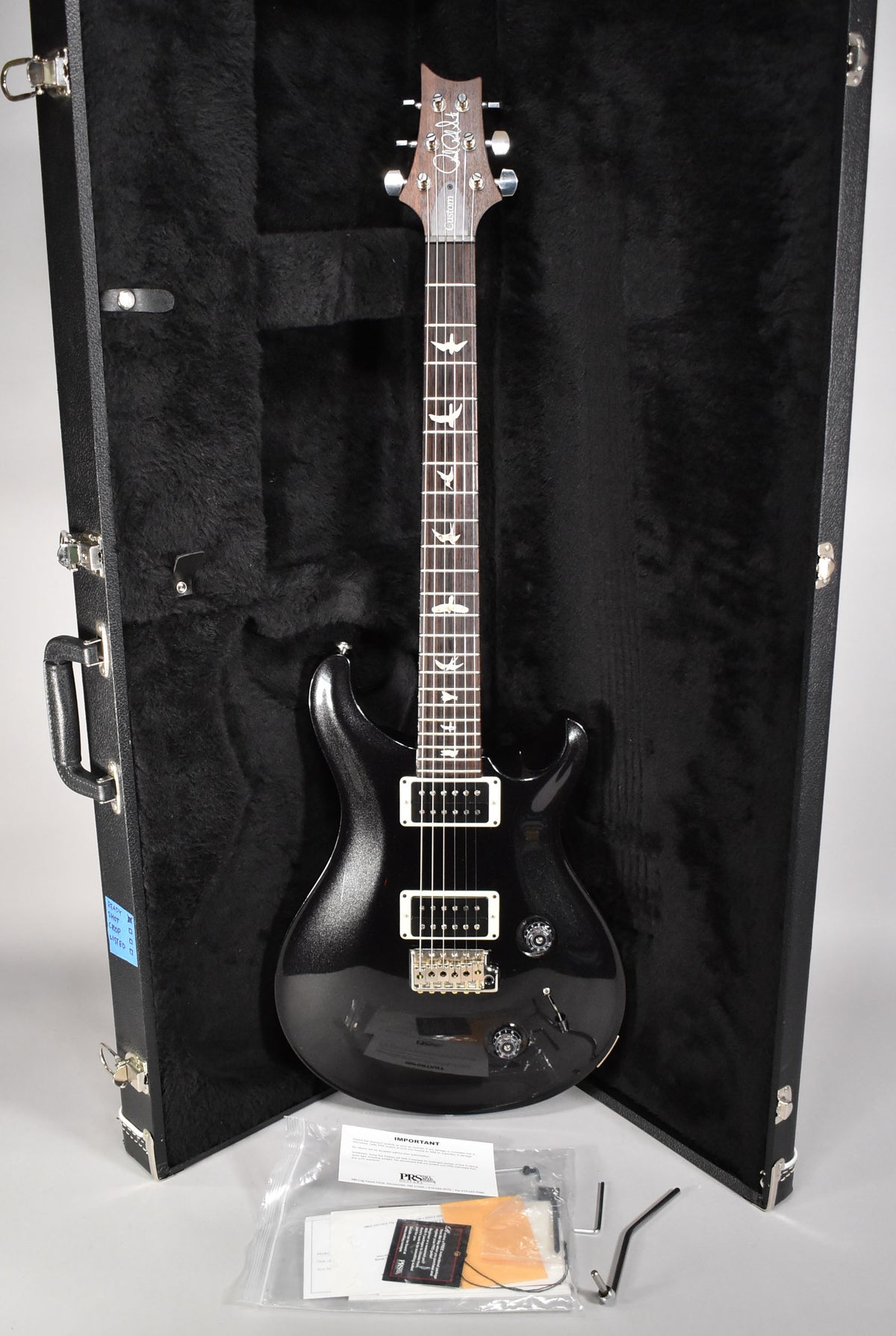 Full-length view of a black sparkle electric guitar with bird inlays, gold hardware, and two humbuckers, resting in its open hard case.