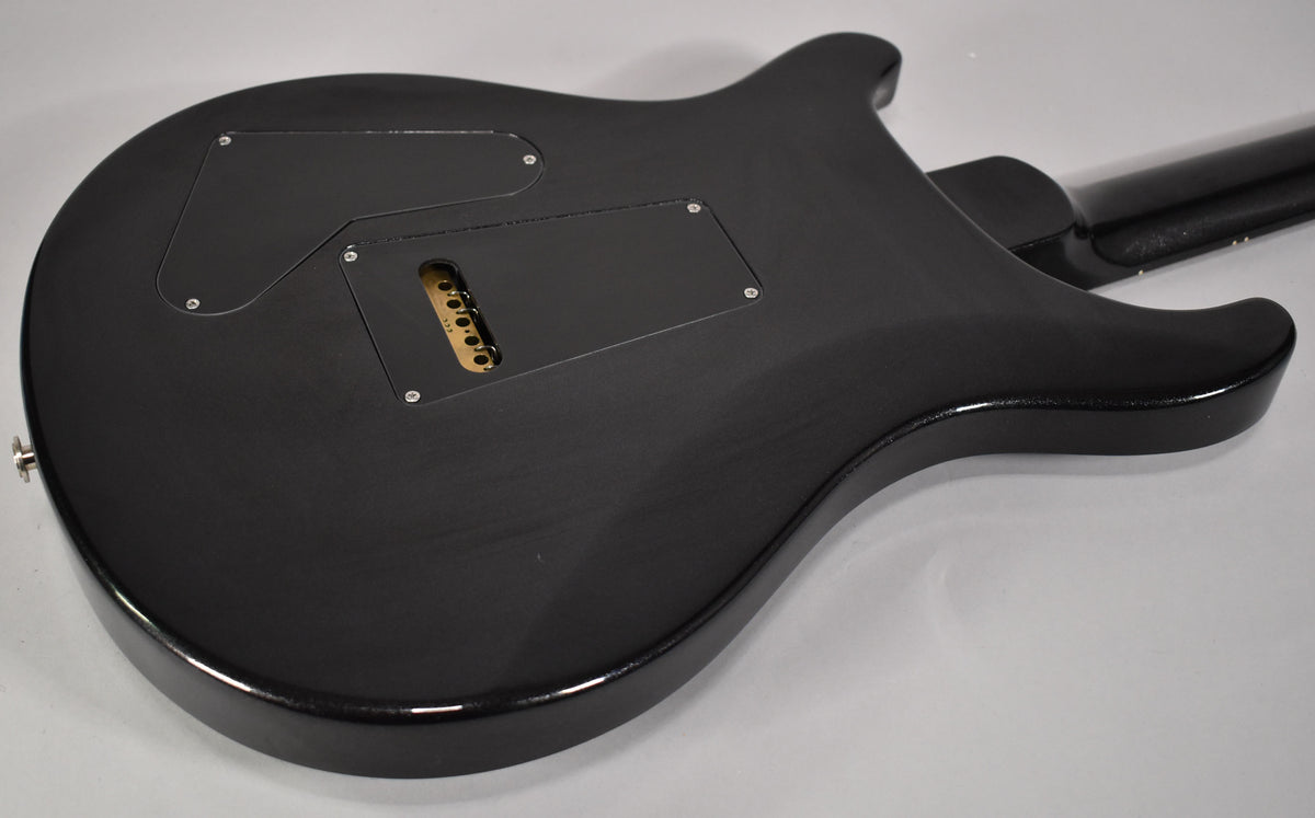 Rear view of a black solid body electric guitar, showing a matte finish with glossy edges and a gold tremolo block.