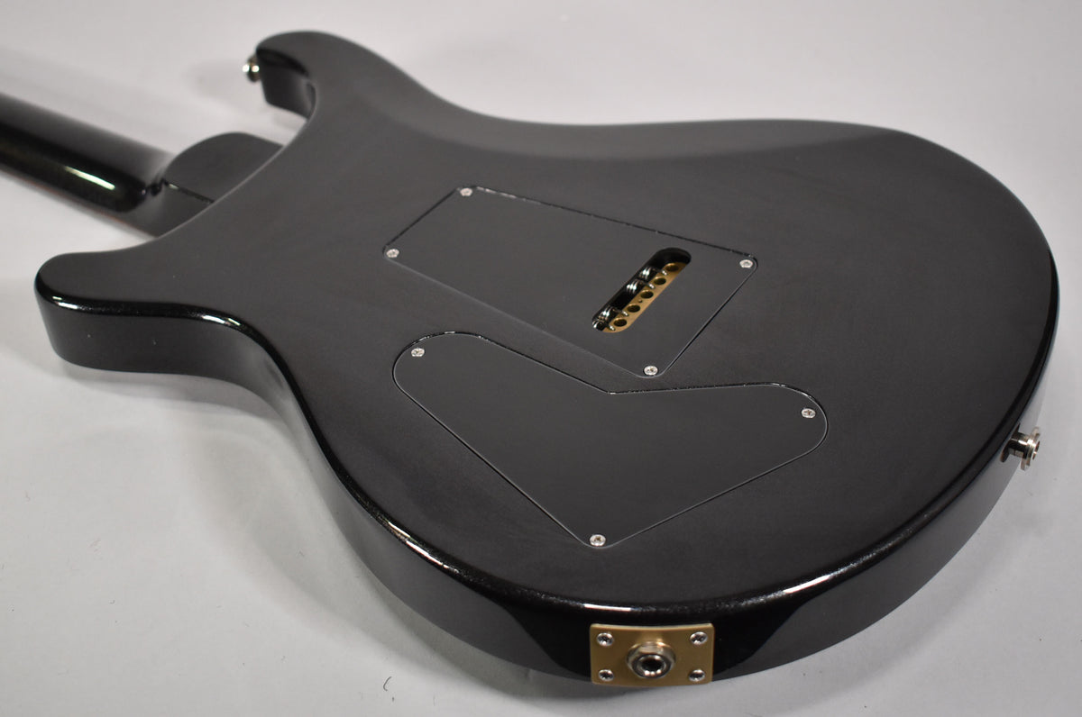 The guitar's glossy black back shows two control cavity covers, a tremolo spring cavity, and a gold output jack plate.