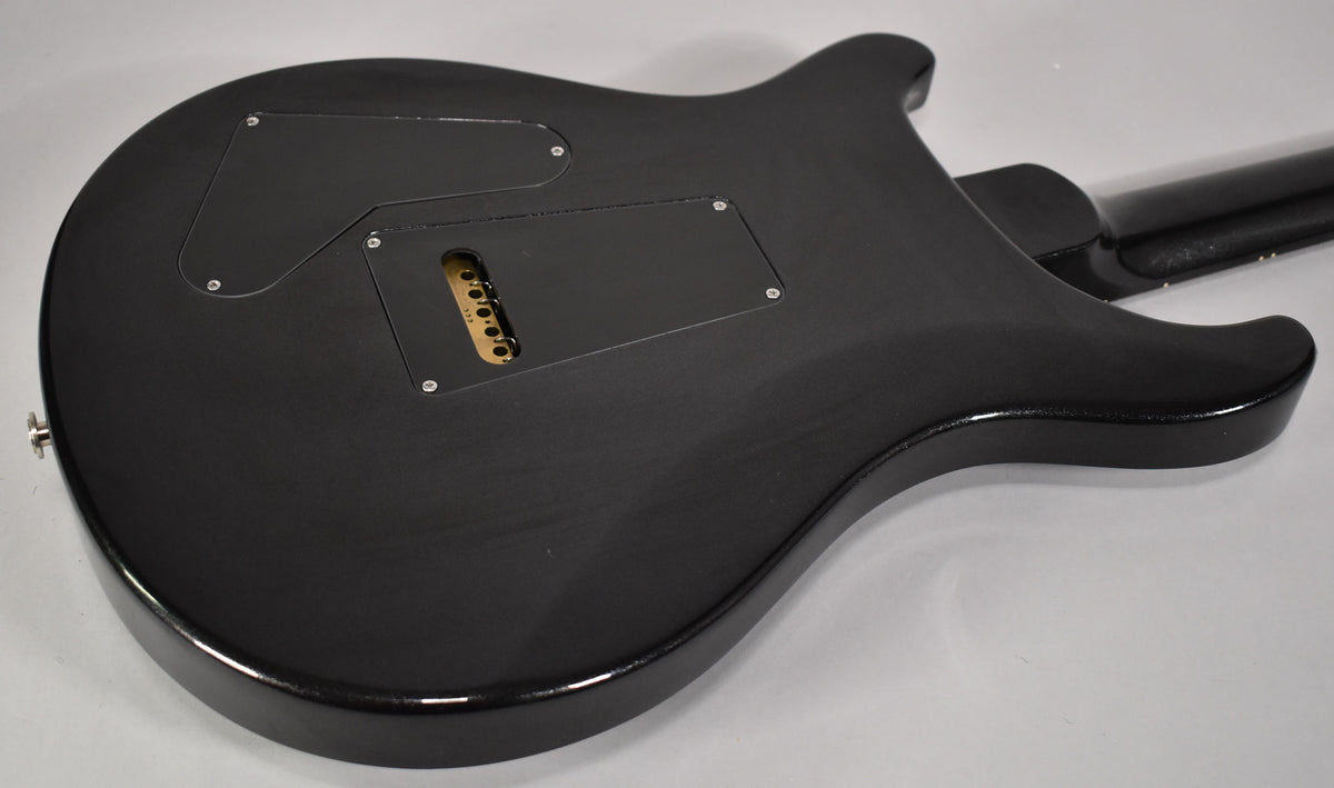 The guitar's black matte back shows two control cavity covers and a gold tremolo block, with a glossy black edge.