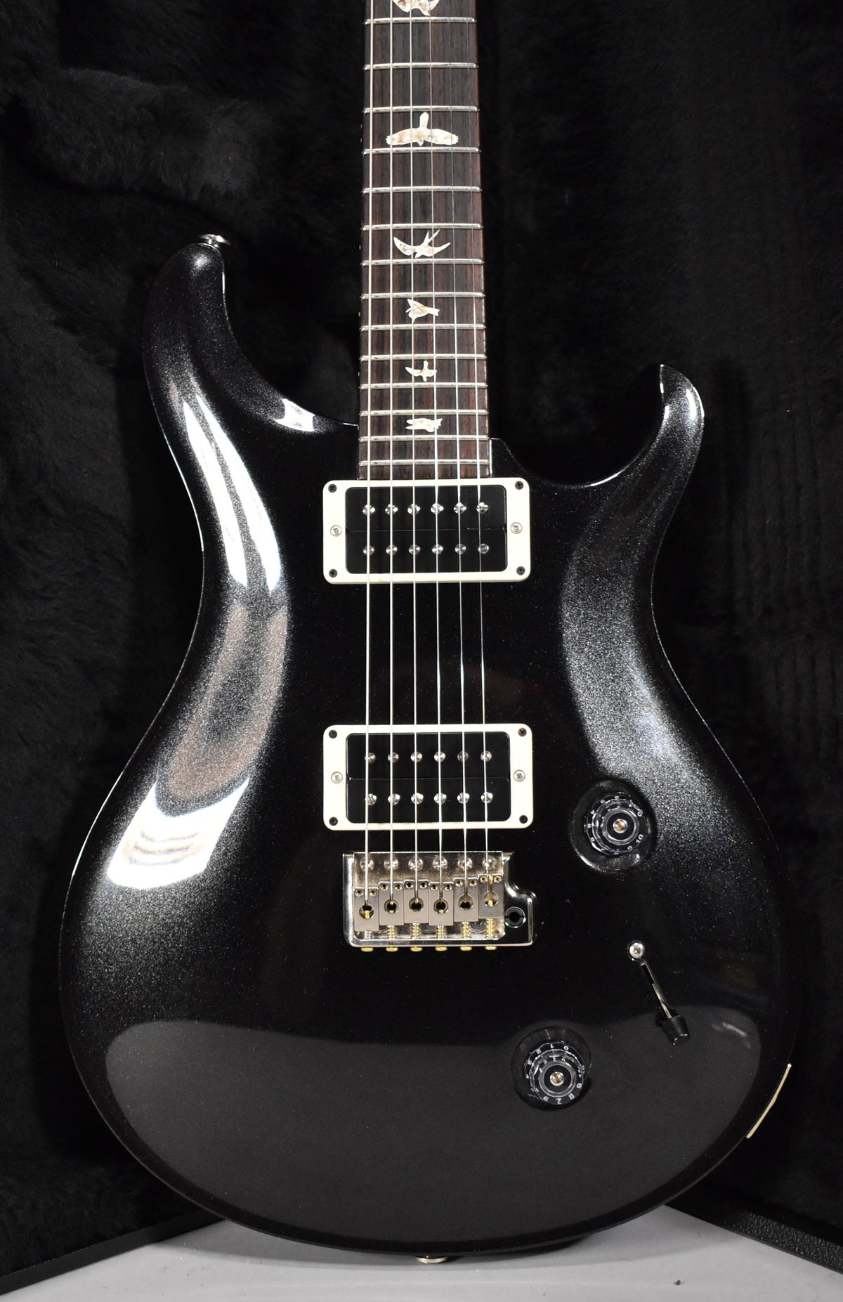 Full-frame view of a black sparkle solid-body electric guitar with white pickup surrounds, bird inlays, and a tremolo bridge.