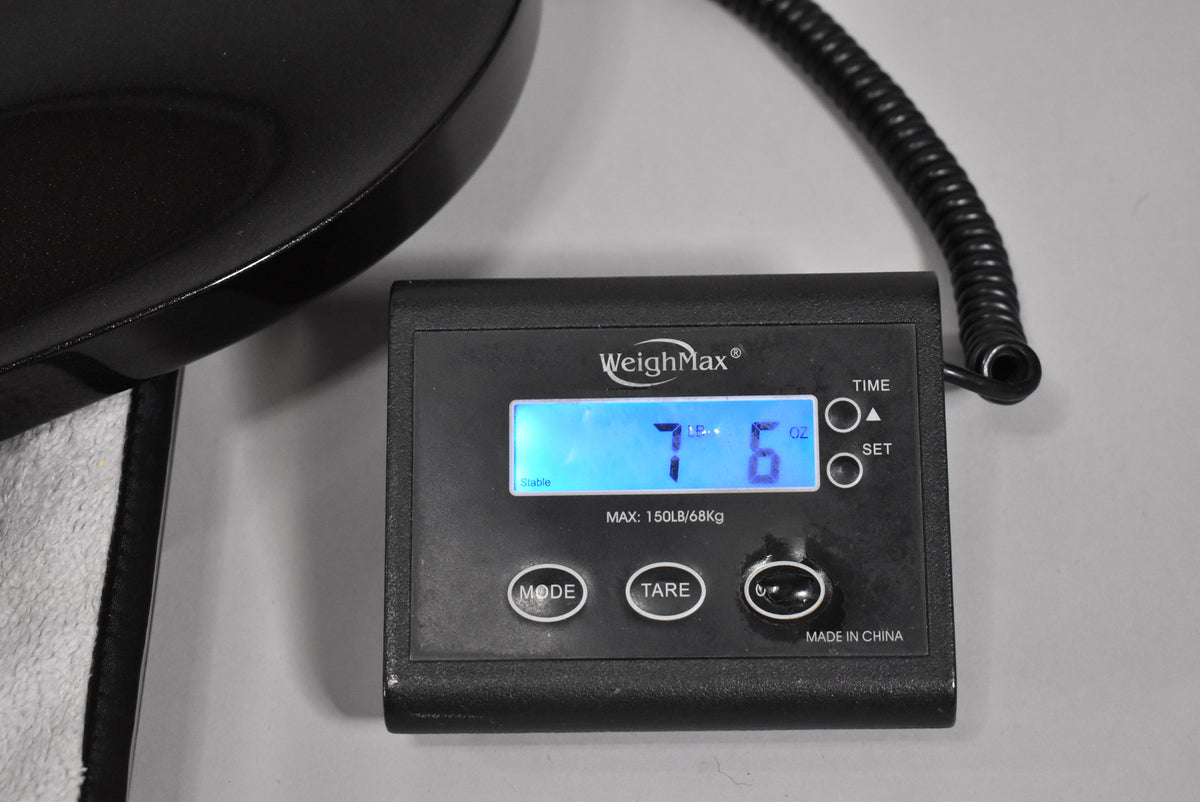 Close-up of the guitar's black body resting on a digital scale, displaying "7 LB. 6 OZ." on a blue backlit screen.