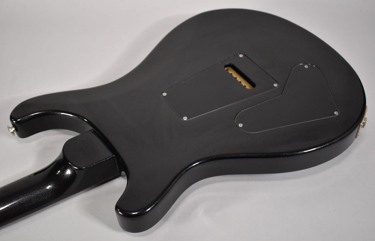 The back of the black solid body guitar shows a matte finish, two control cavity covers, and a tremolo spring cavity with a wooden block.
