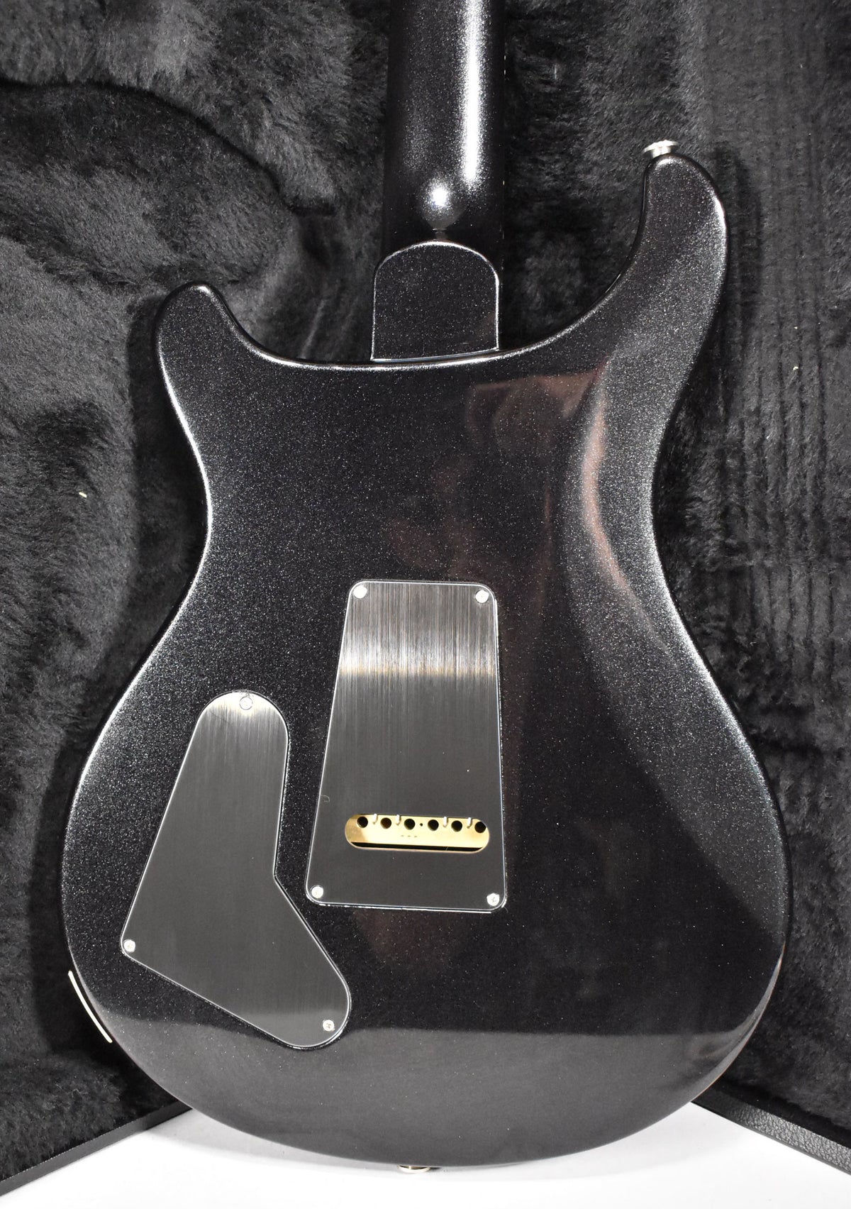 The guitar's black sparkle back, with two clear control cavity covers and six gold string ferrules, rests in a black fur-lined case.