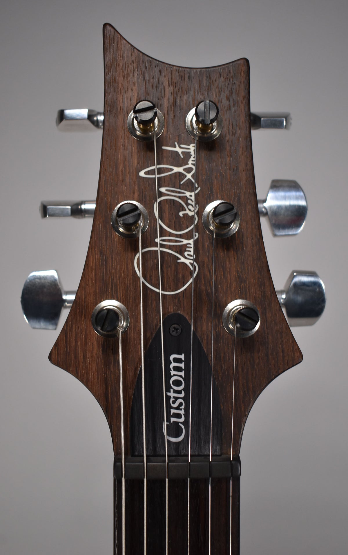 Close-up of the dark brown wooden headstock with six chrome tuners, showing the white script logo and black truss rod cover.