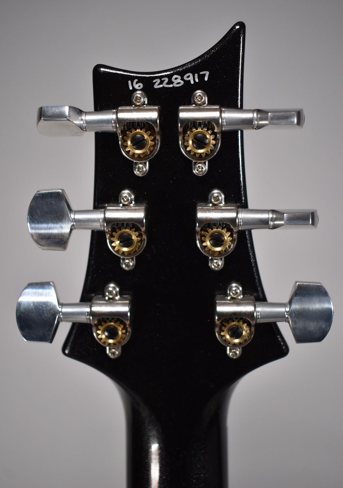 Rear view of the black headstock and neck, showing six silver tuning pegs with visible brass gears.