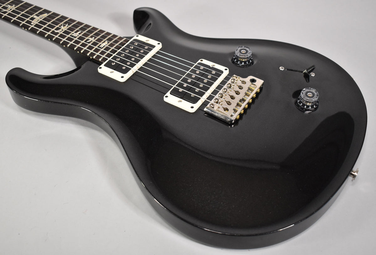 The black sparkle finish guitar body is angled from the upper left, showing white-bobbin humbuckers and a tremolo bridge.