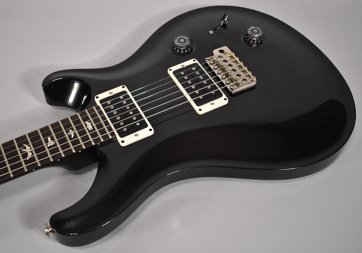 Close-up of a black sparkle electric guitar body with white humbucker pickups, chrome hardware, and bird inlays on the fretboard.
