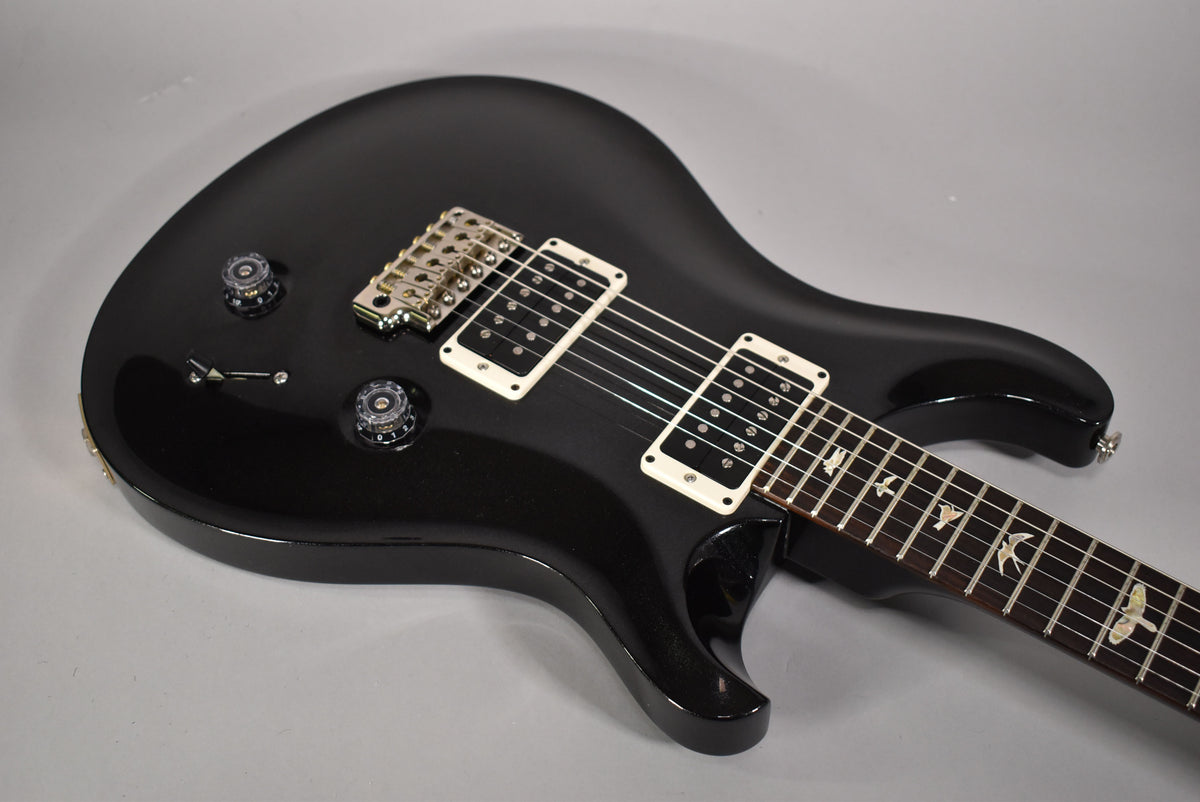 Black solid body electric guitar, angled from above, showing the upper bout, two white-framed humbuckers, and bird inlays on the fretboard.