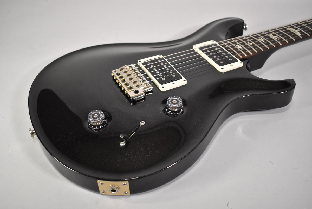 Black solid body electric guitar, angled from the lower bout, showing two cream humbuckers, a chrome bridge, and two clear control knobs.