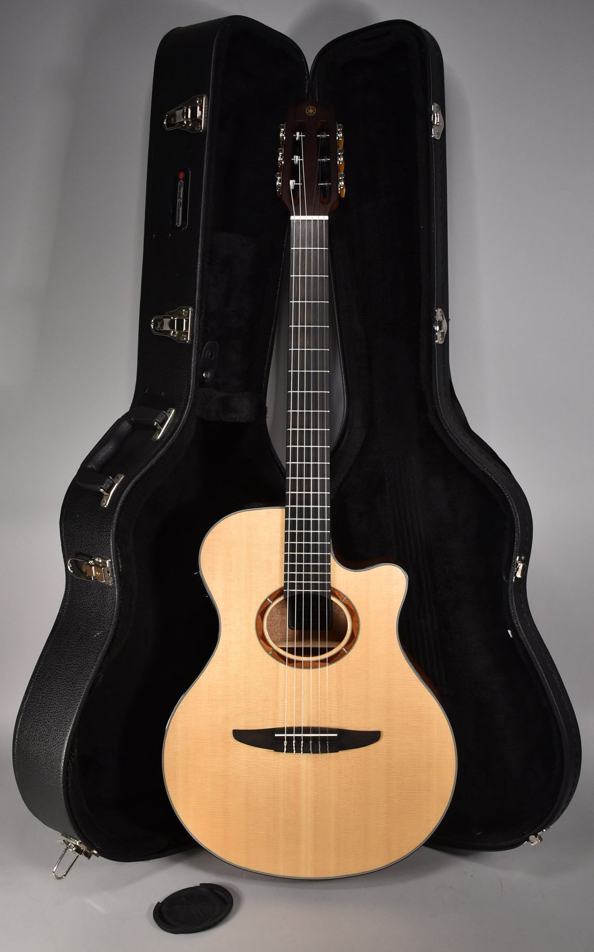 A light-wood classical guitar with a cutaway body and dark rosette stands upright between two open hard cases.