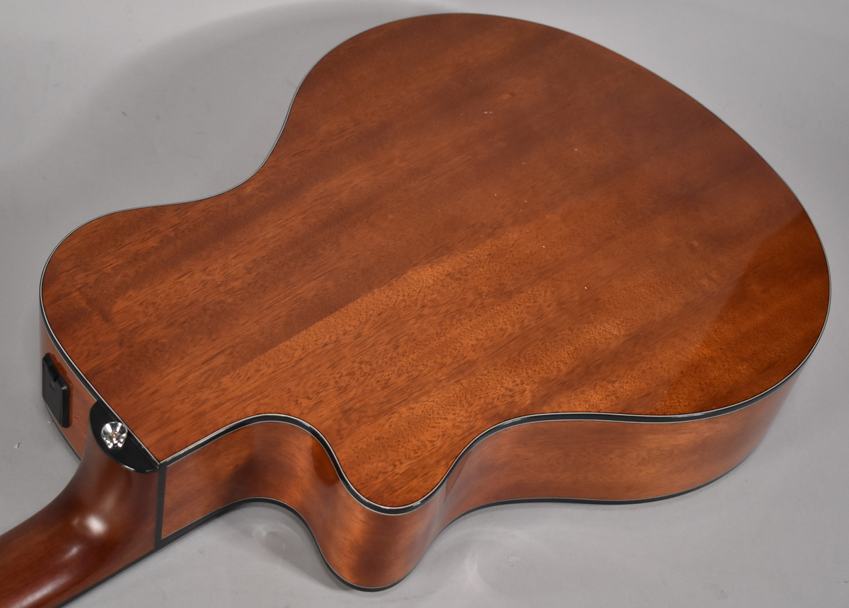 The back of a classical electric guitar, showing its reddish-brown wood grain, cutaway, and a chrome strap button near the neck heel.