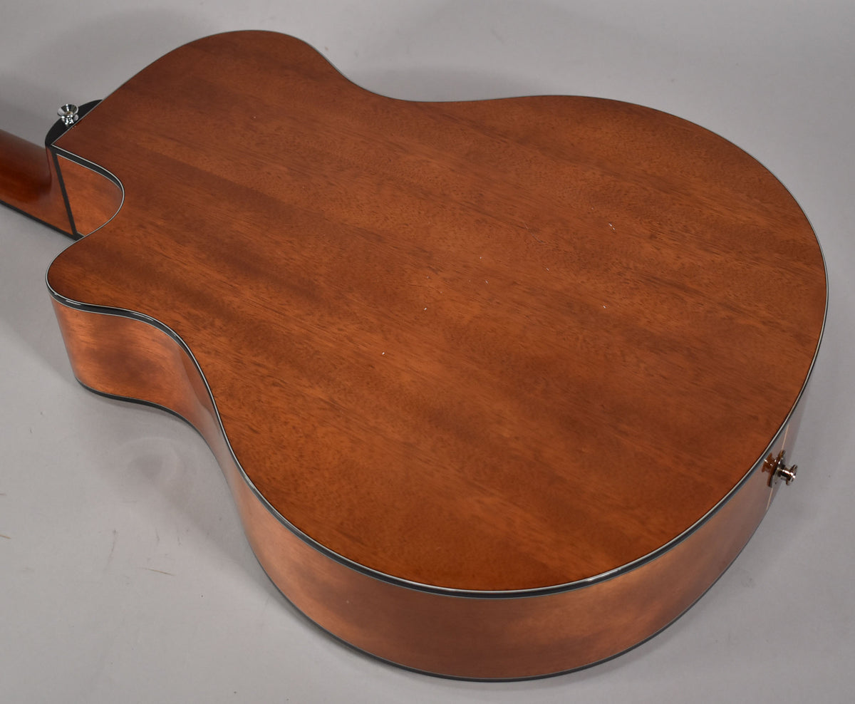 View of the guitar's reddish-brown back and sides, showing a cutaway and endpin jack, with minor surface scuffs.