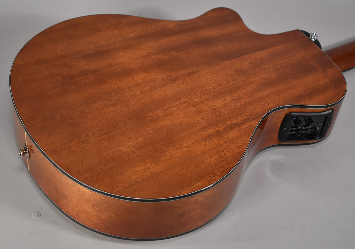 The back of a classical guitar with a cutaway, showing a warm brown wood grain and a black control panel on the upper bout.